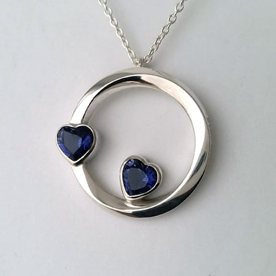 Double hearts mobius infinite open cirkle shape pendant shiny finish sterling silver and two heart shaped faceted iolite gemstones Daphne Meesters Jewellery Designer Goldsmith The Hague Netherlands