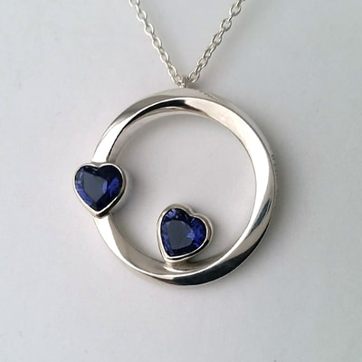 Double hearts mobius ring shaped pendant shiny finish sterling silver and two heart shaped faceted iolite gemstones Daphne Meesters Jewellery Designer Goldsmith The Hague Netherlands